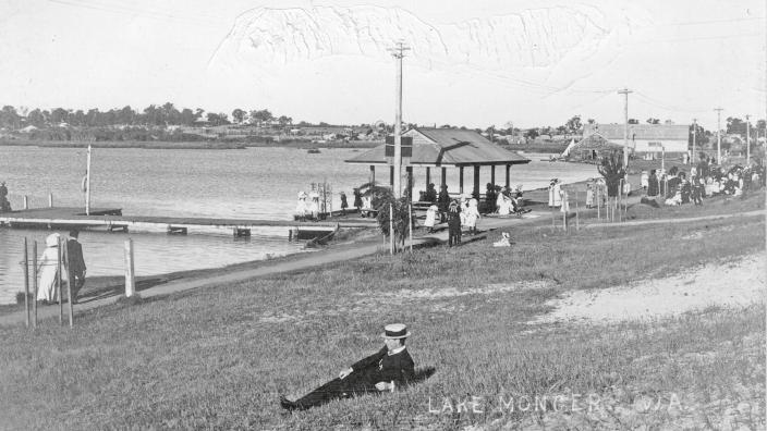 Black and white photo of lake with grassland and man lying down 